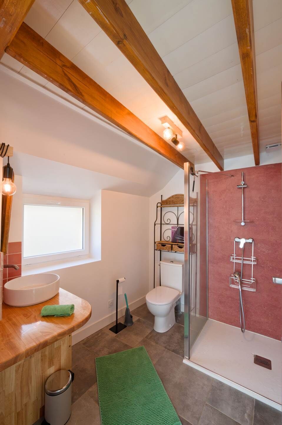 A bathroom with a wooden ceiling, a glass shower enclosure, a toilet, and a sink with a green towel.