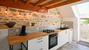 A kitchen with a stone wall, wooden beams, a wooden countertop, and a skylight.