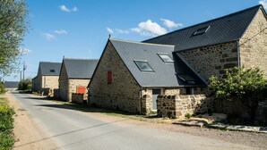 A row of stone buildings with pitched roofs and skylights, situated along a rural road.