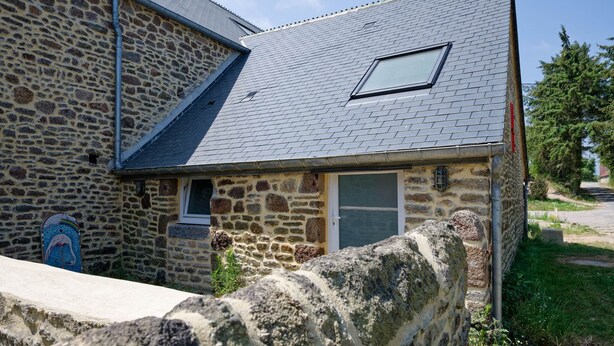 A stone building with a sloped roof, a small window, and a door.