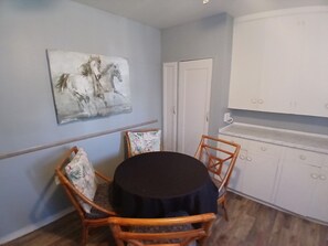 Uma área de jantar com mesa redonda, quatro cadeiras, pintura de cavalos, porta branca e armário branco.