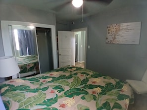 Un dormitorio con cama, puerta, espejo, una obra de arte en la pared y un ventilador de techo.
