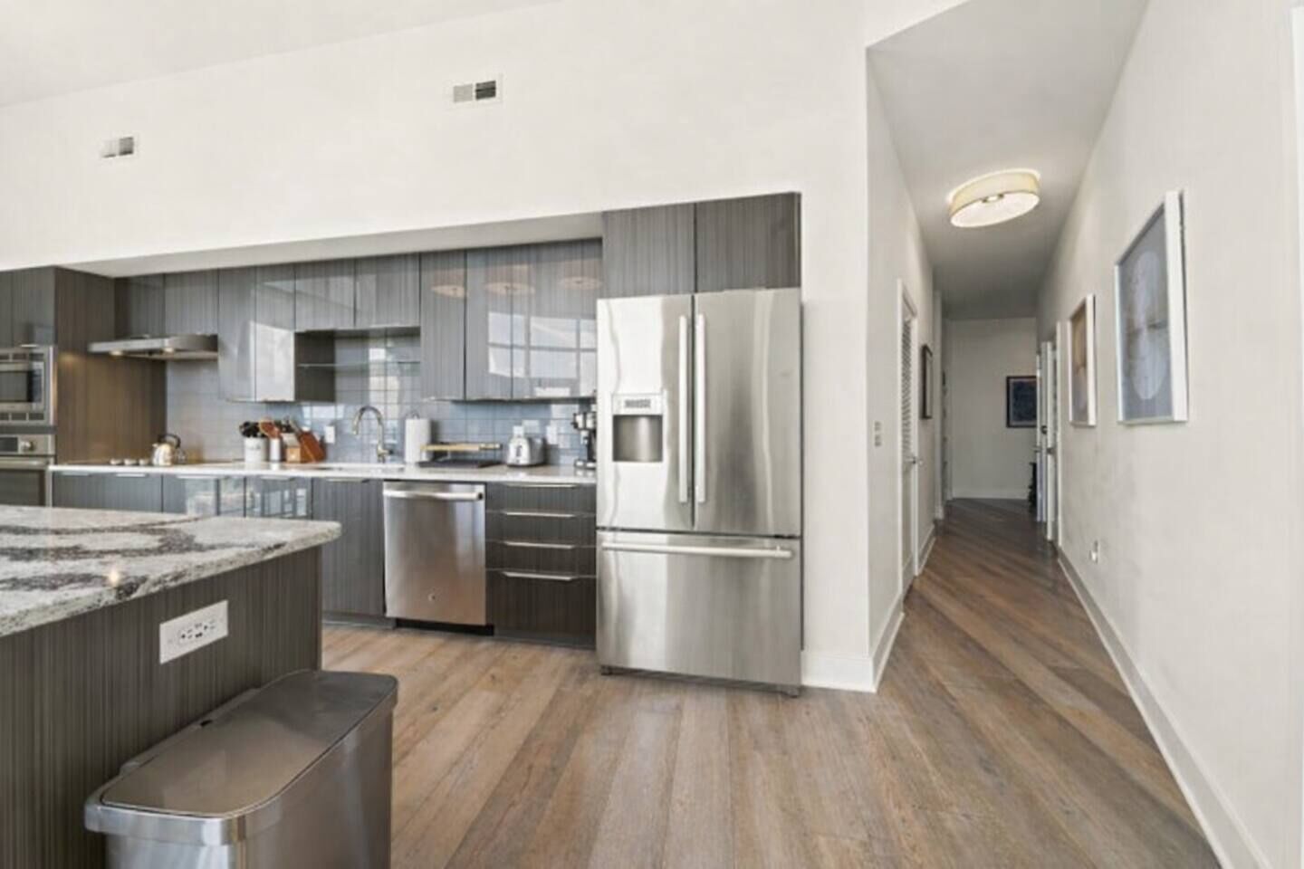 A modern kitchen with stainless steel appliances, a marble countertop, and wooden flooring.