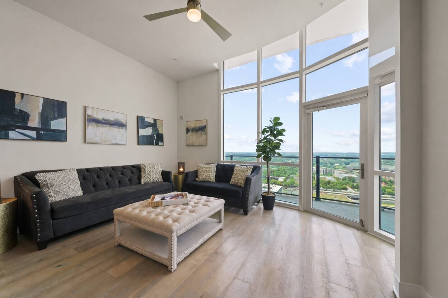 A spacious living room with a large window, a ceiling fan, and a black leather sofa.