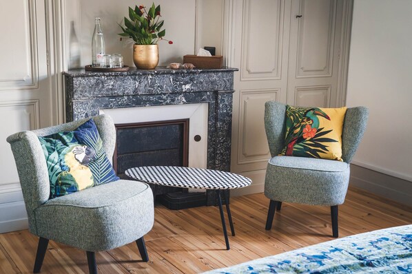 A room with two armchairs, a small round table, a fireplace, and a potted plant.