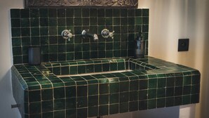 Casa de banho com lavatório em azulejos verdes e duas torneiras.