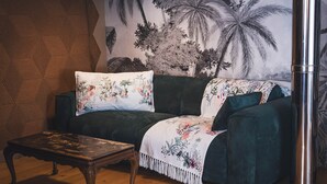Een woonkamer met een donkergroene bank, een houten salontafel en een muurschildering van palmbomen.