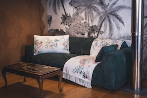 Una sala de estar con un sofá verde oscuro, una mesa de centro de madera y un mural de palmeras en la pared.