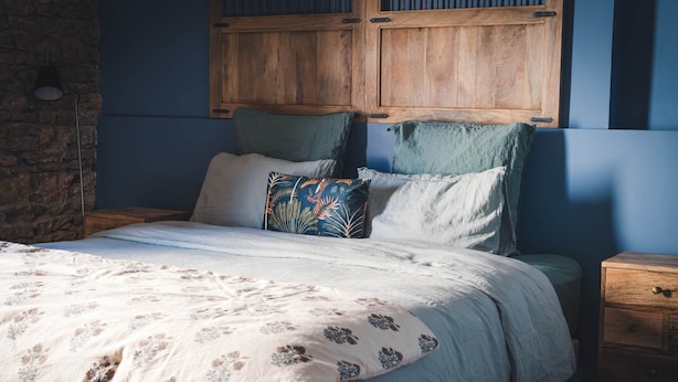 Un dormitorio con cama, almohadas, cabecera de madera, mesita de noche y lámpara.