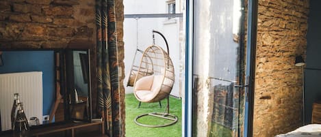 Une pièce avec un mur en pierre, un fauteuil suspendu, une porte vitrée et une vue sur un espace verdoyant.