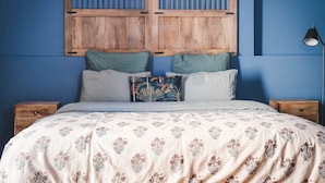 Un dormitorio con cama, almohadas, una mesita de noche, lámpara y cabecera de madera.