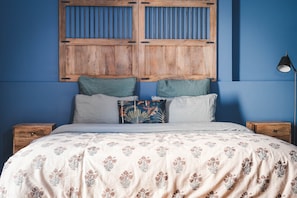 Une chambre à coucher avec un lit, des oreillers, une table de chevet, une lampe et une tête de lit en bois.