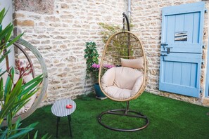 A wicker hanging chair with cushions, a small round table with a red object, and a blue door with a sign. - Les Jardins de Cormatin Room (FUISSE)