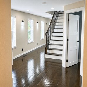 Ein geräumiger Flur mit Holzboden, einer Treppe mit schwarzer Geländer und einer weißen Tür.