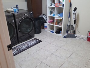 Ein Waschraum mit zwei LG Frontlader-Waschmaschinen, einem Regal für Reinigungsmittel und einem Besen.