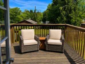 Une terrasse en bois avec deux fauteuils en osier et une petite table, le tout entouré d’une balustrade en bois.