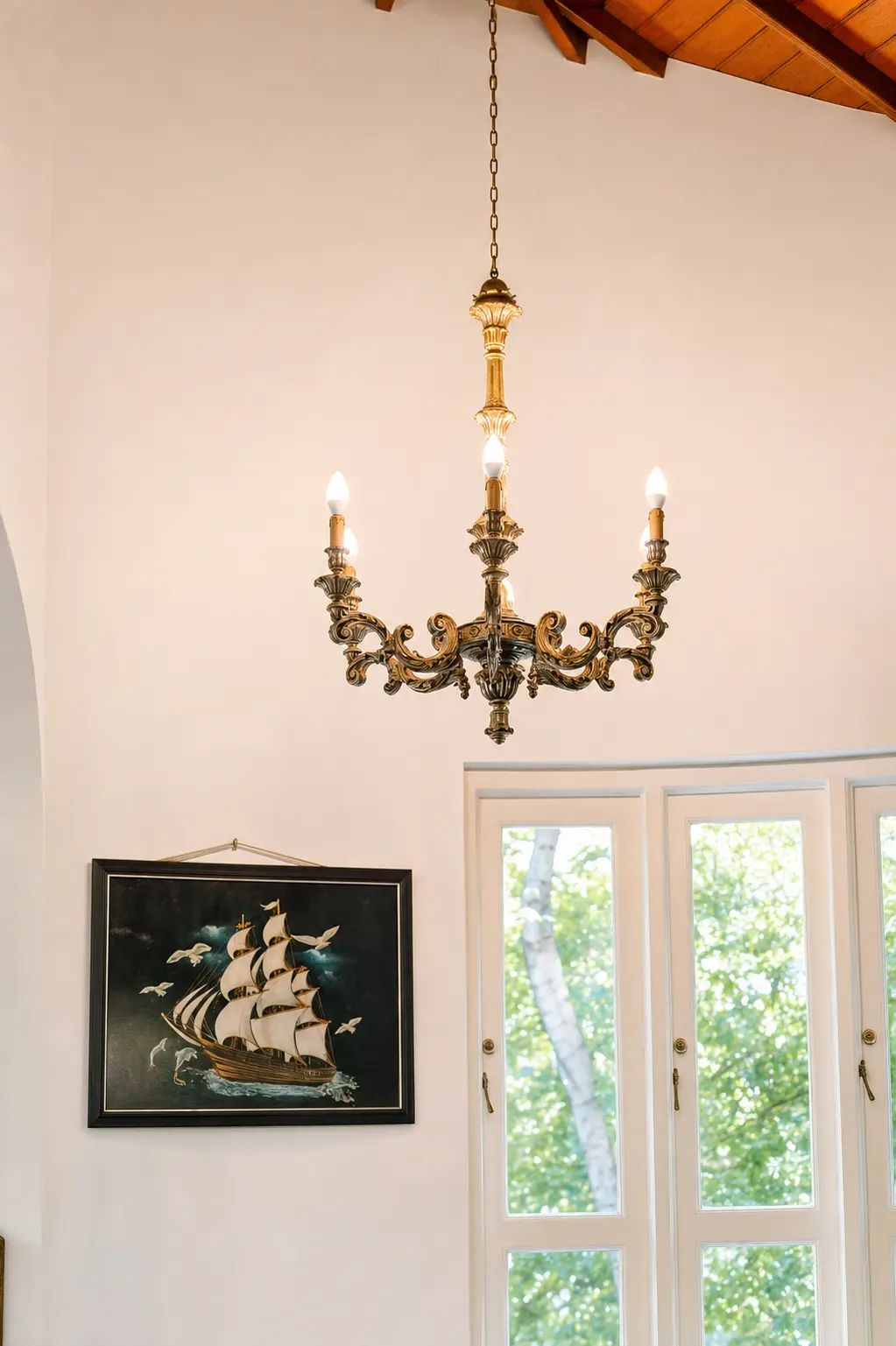 A chandelier with multiple candle-like lights, a framed maritime painting, and a white door with glass panels.