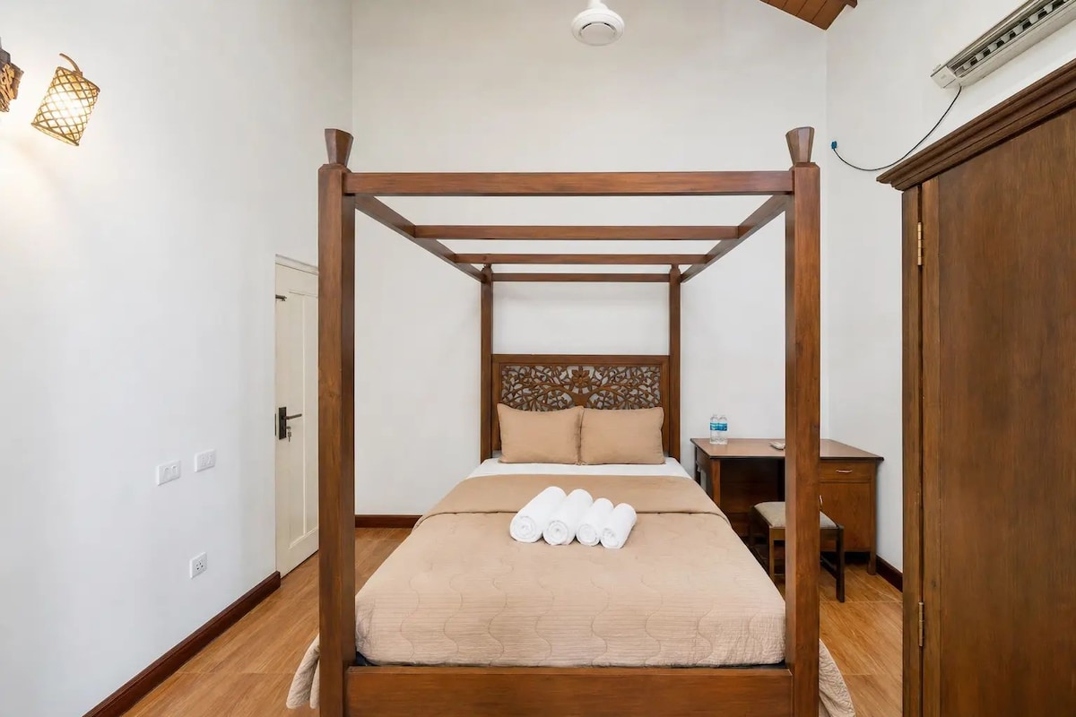 A four-poster bed with a headboard, a bedside table, and a water bottle on the nightstand.
