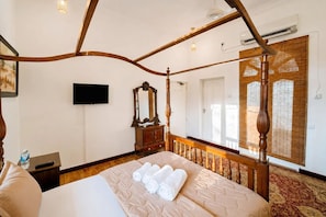 A four-poster bed with rolled towels, a wooden dresser, a flat-screen TV, and a large window with bamboo blinds. - Skyport Villa Negombo (Negombo)