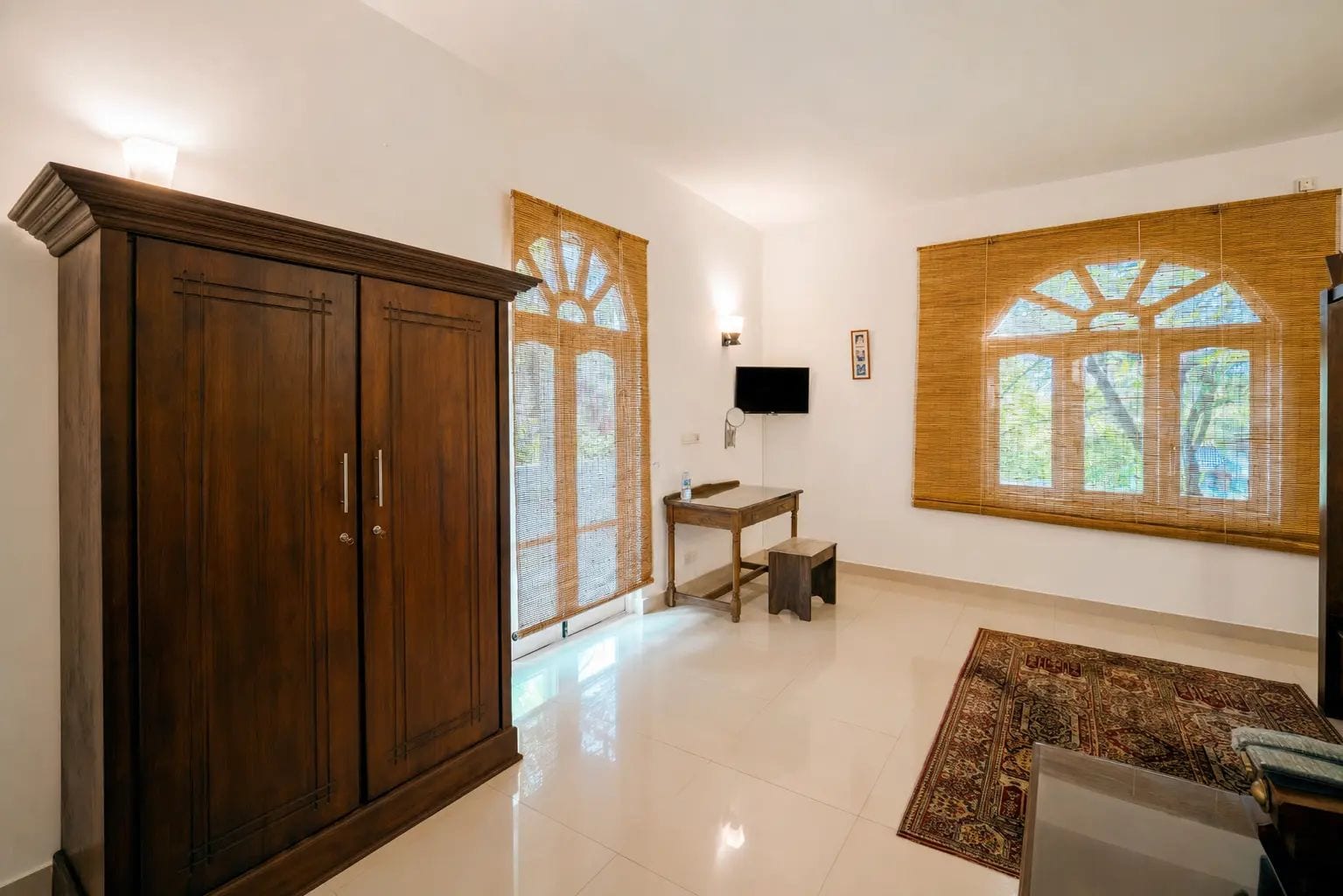 A spacious room with a large wooden wardrobe, a small desk, a television, and a large window with a view.