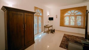 A room with a wooden wardrobe, a small table, a television, and a window with bamboo blinds. - Skyport Villa Negombo (Negombo)