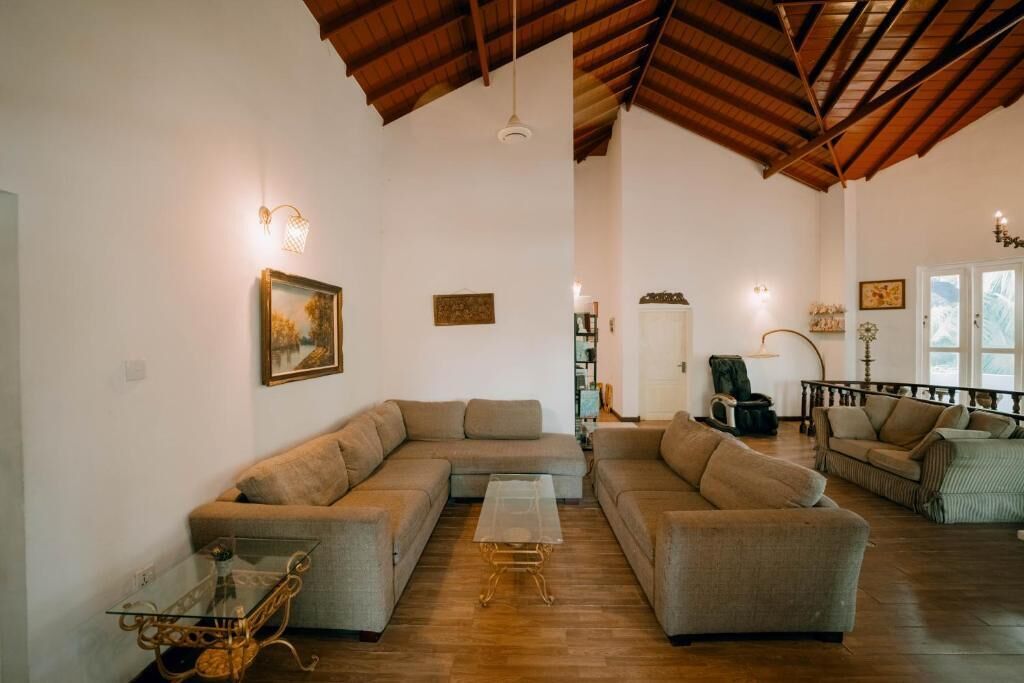 Ein großzügiges Wohnzimmer mit hohen Decken und Holzbalken, ausgestattet mit einem großen L-förmigen Sofa, einem Glastisch und einem Korbtisch.