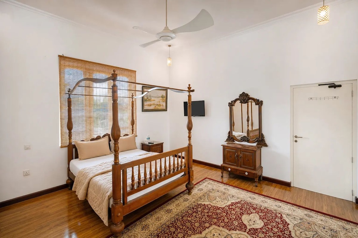 A bedroom with a four-poster bed, a wooden wardrobe, a mirror, a television, and a door with a lock.