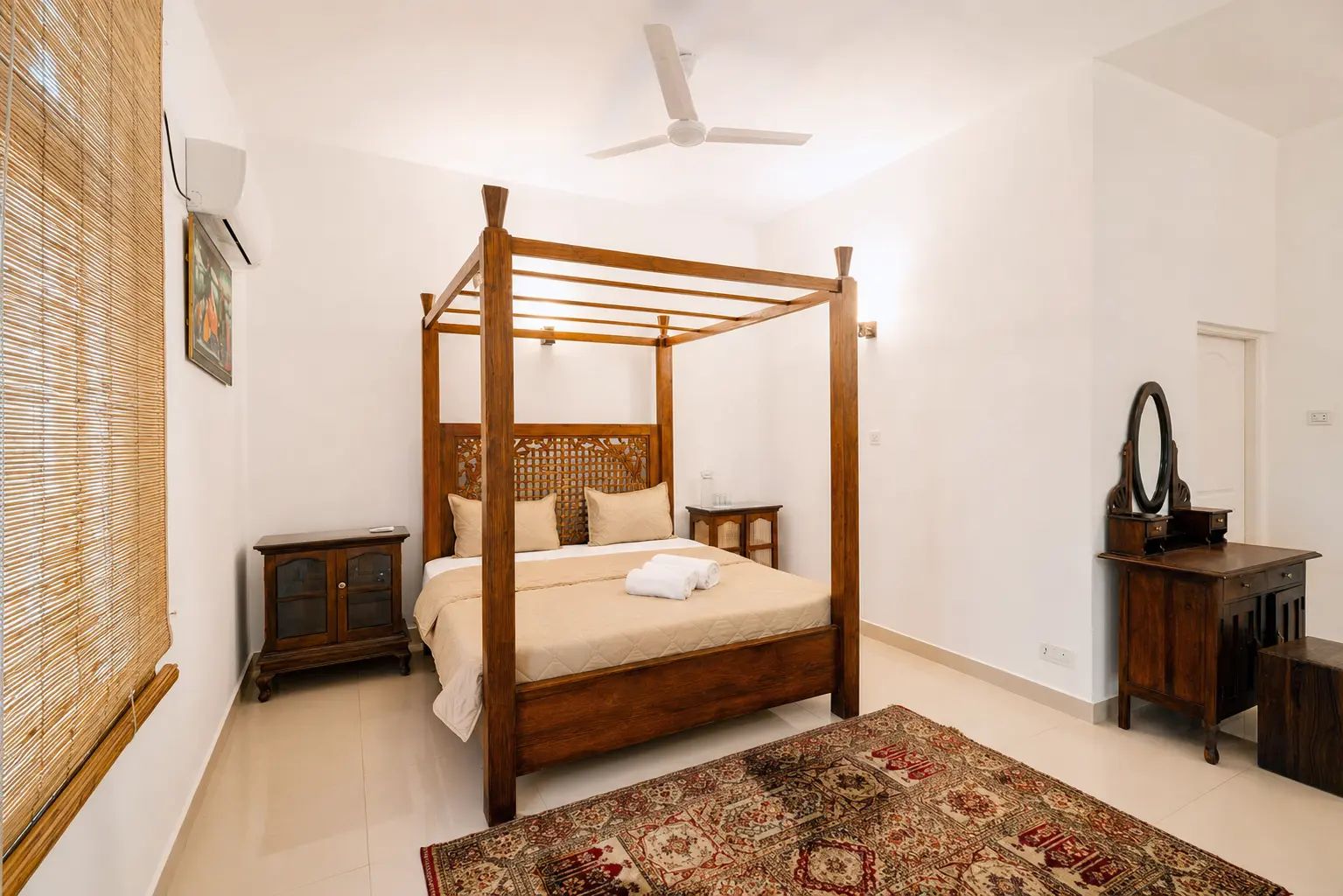 A four-poster bed with a wooden frame, a bedside table, a mirror, and a patterned rug in a hotel room.