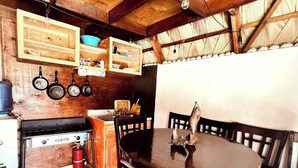 A rustic kitchen with wooden beams, a gas stove, hanging pots, and a round wooden table with chairs. - "El Nirvana" Oceanfront Cabin: Surf & Desert (Punta Abreojos)