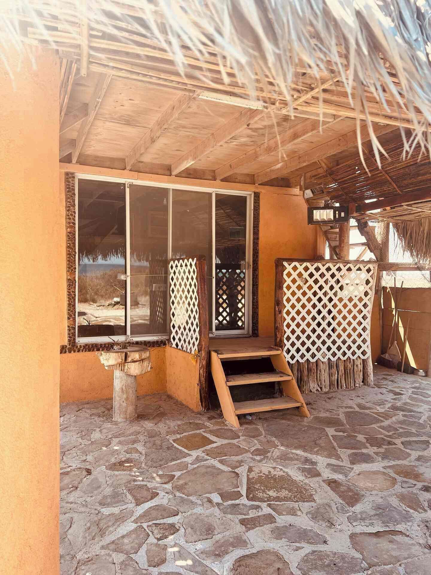 Un espace extérieur abrité, doté d’un sol en pierre, d’escaliers en bois et d’un toit de chaume.