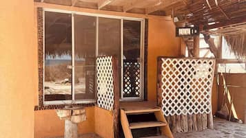 Un espace extérieur abrité, doté d’un sol en pierre, d’escaliers en bois et d’un toit de chaume.