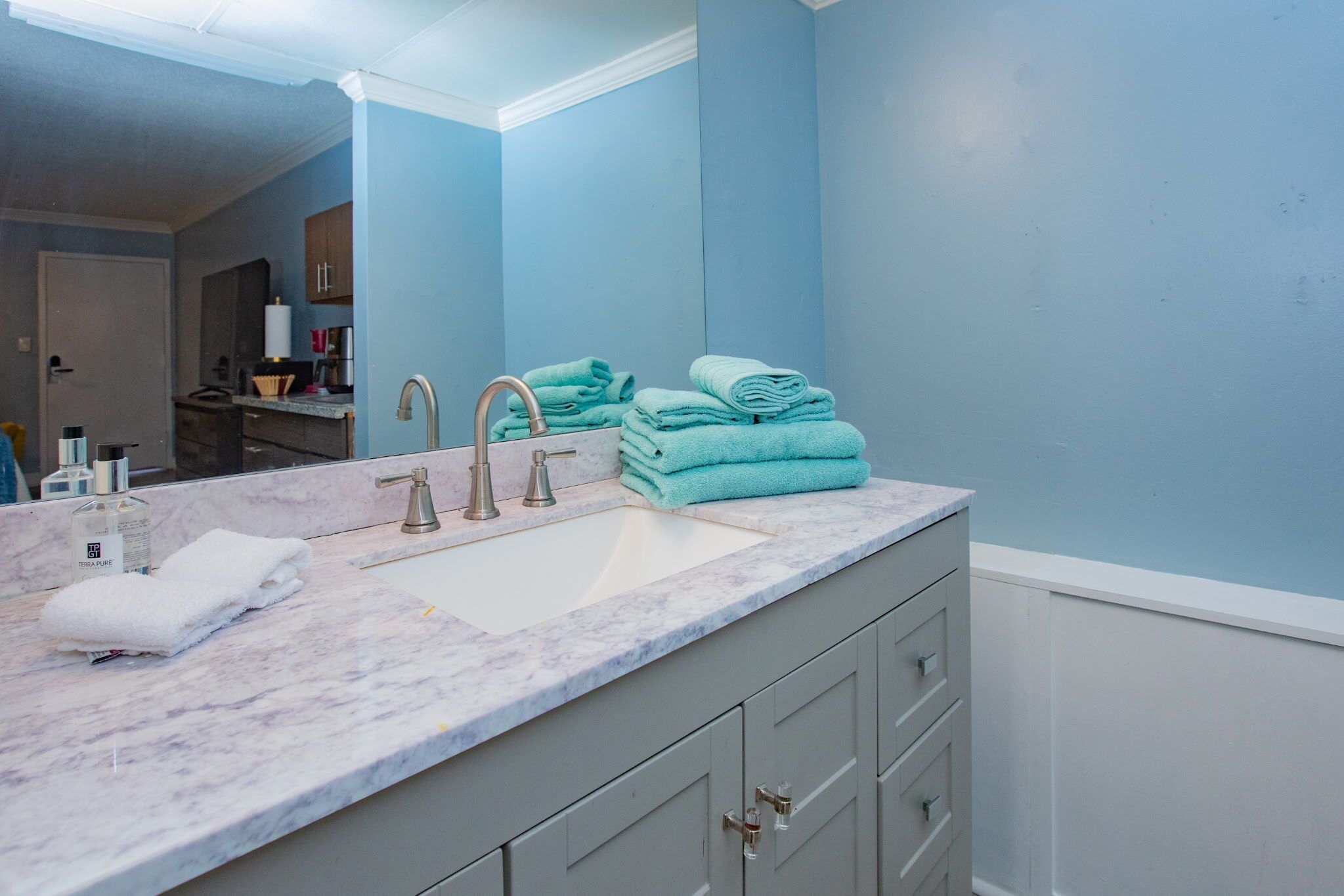 A bathroom with a marble sink, two faucets, a mirror, and a stack of folded towels.