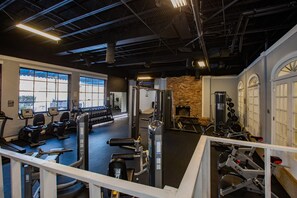 A gym with various exercise equipment, large windows, and a brick wall. - Lux Mins To @ Atrium Health@ CLT @ Bojangles Stadium (Charlotte)