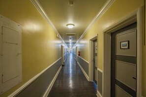 A hotel hallway with doors on both sides, a fire extinguisher, and a number sign on the right door. - Lux Mins To @ Atrium Health@ CLT @ Bojangles Stadium (Charlotte)