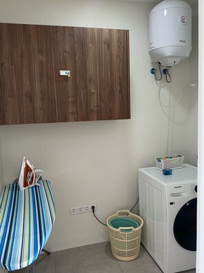 Ein Waschraum mit Waschmaschine, Trockner, einem Holzschrank und einem an der Wand montierten Warmwasserbereiter.