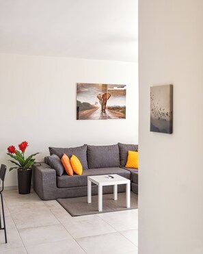A modern living room with a grey sofa, a white coffee table, and a painting of a landscape. - Nice View Apt 5 - 2-BR apartment with AC on spectacular Mahuma hill (Mahuma (Curacao-Middle))
