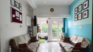 A living room with a sofa, a coffee table, and a TV. There is a door leading to a balcony. - Eden Paradisee (Ootacamund)
