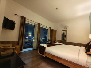 Habitación de hotel con cama, escritorio, silla, televisión y vista de la ciudad de noche.