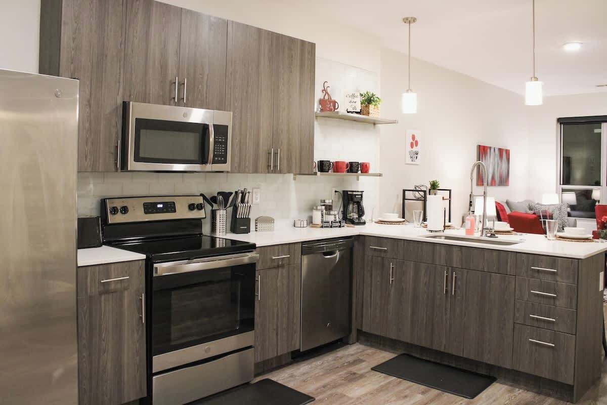 Una cocina moderna con electrodomésticos de acero inoxidable, gabinetes de madera y una encimera blanca.