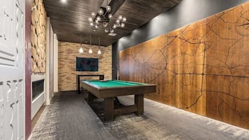 Una sala de billar con mesa de pool, pared de madera con diseño de mapa e iluminación colgante.