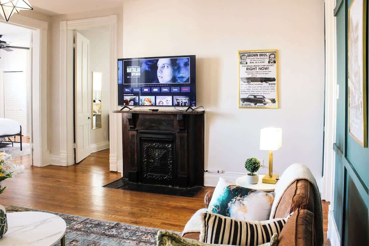 Una sala de estar con chimenea, un televisor montado arriba y un cartel enmarcado en la pared.