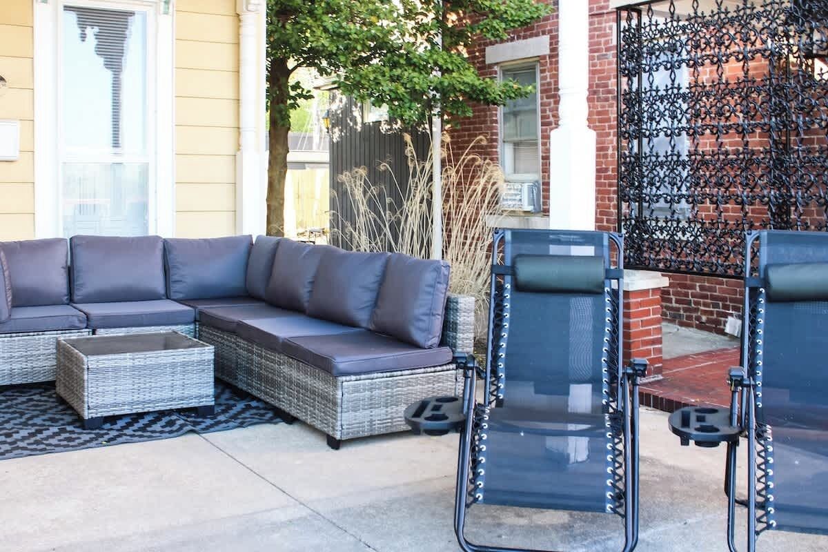 Un patio con un sofá seccional gris, dos sillones de mimbre y una pequeña mesa.