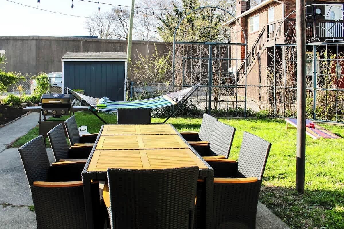Un patio al aire libre con una mesa de madera y sillas de mimbre, una hamaca y una cerca de metal.