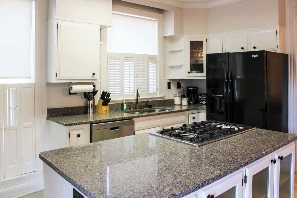 Una cocina moderna con encimeras de granito, un refrigerador negro y muebles blancos.
