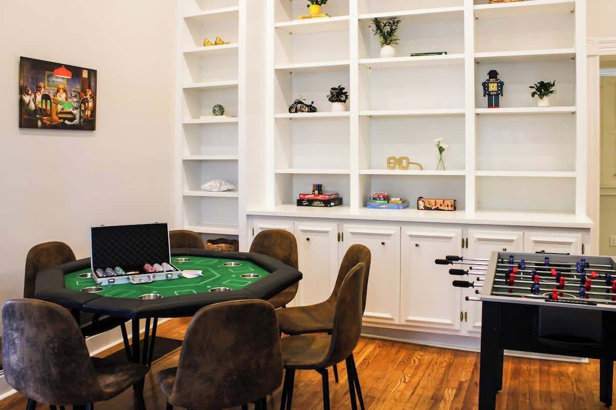 A room with a green felt table for foosball, a poker table, and a bookshelf with various items.