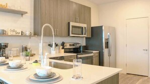 A modern kitchen with a central island, stainless steel appliances, and wooden cabinetry. - Walk to Bars & Dining — Free Parking & Gym (Louisville)