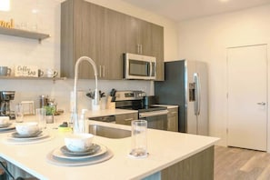 A modern kitchen with a central island, stainless steel appliances, and wooden cabinetry. - Walk to Bars & Dining — Free Parking & Gym (Louisville)