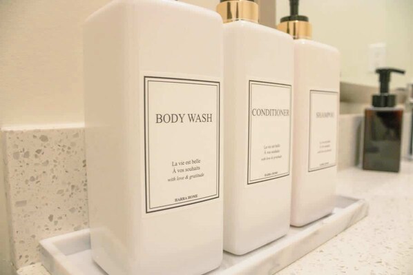 Trois flacons de gel douche et d’après-shampoing sont posés sur le comptoir d’une salle de bain.