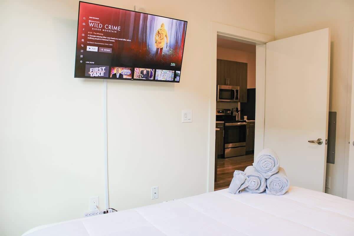 A hotel room with a bed, a TV mounted on the wall, and a door leading to a kitchenette.