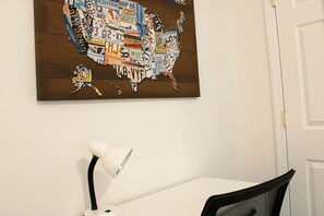 Eine an der Wand hängende Karte der Vereinigten Staaten aus Autokennzeichen, ein weißer Schreibtisch und ein schwarzer Stuhl mit Mesh-Gepolsterung.